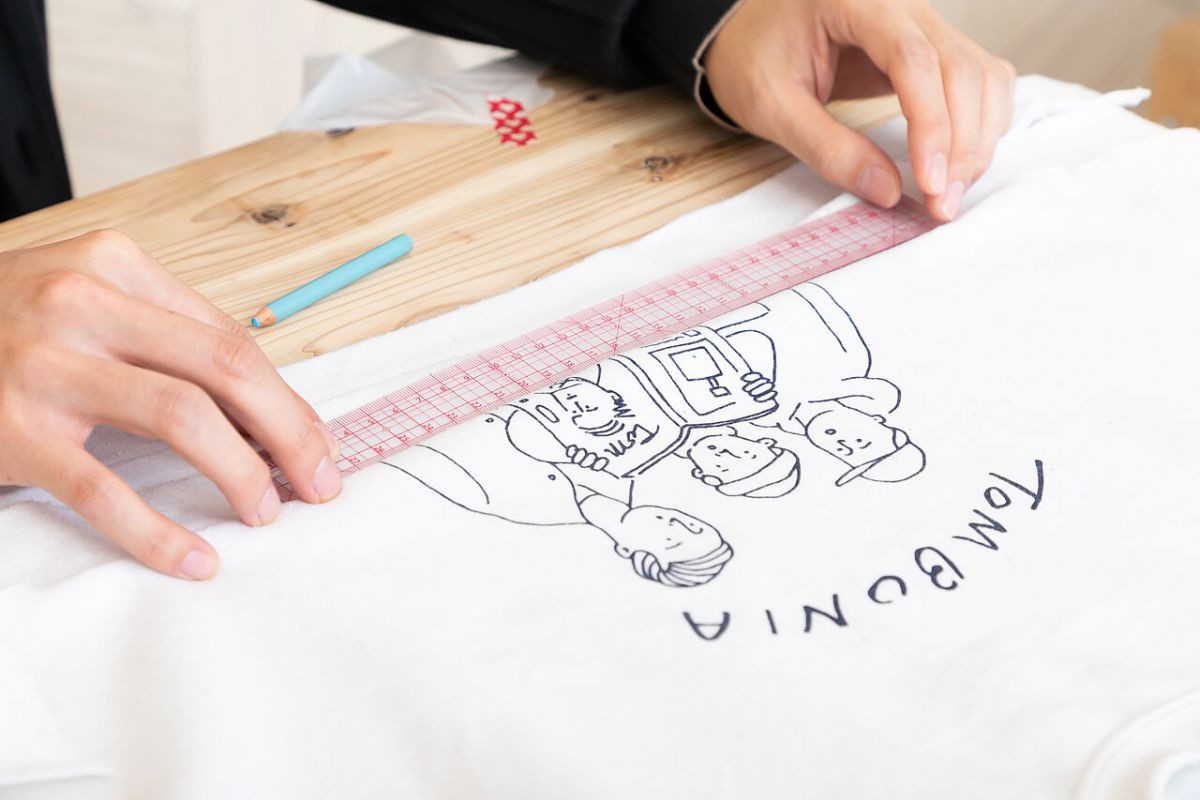 アイロンで伸ばしたトレーナーの中央を測り、帽子のサイズ（頭囲−8cm）にカットしていく小関さん