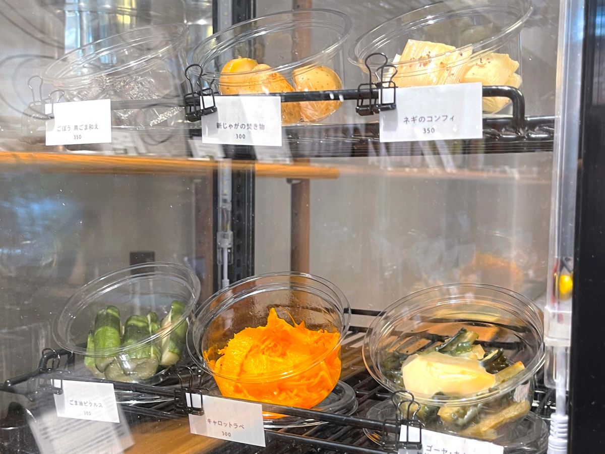 （左上から）ごぼう　黒ごま和え 350円、新じゃがの焚き物 300円、ネギのコンフィ 350円、ごま油ピクルス 300円、キャロットラペ 300円、ゴーヤ・キウイ ねりごま豆腐ソース 400円