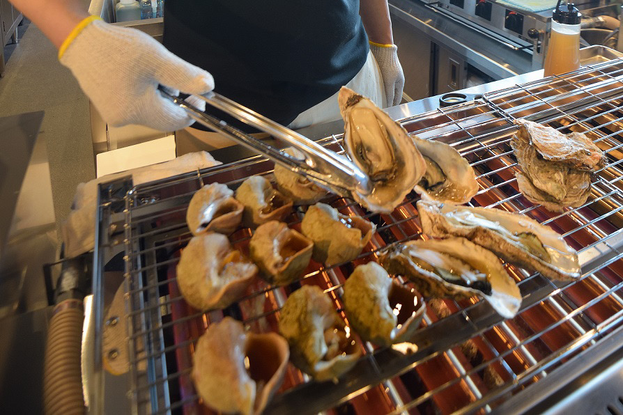 （右）特大 焼き牡蠣1個590円、2個990円、（左）名物焼きつぶ2個590円
