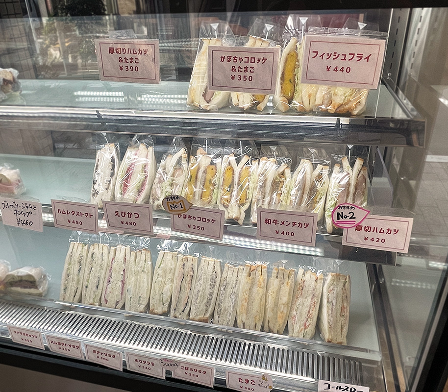 (上段左から)「厚切りハムカツ&たまご」390円、「かぼちゃコロッケ&たまご」350円、「フィッシュフライ」440円、(中段左から)「ブルーベリージャムとホイップ」460円、「ハムレタストマト」450円、「えびかつ」480円、「かぼちゃコロッケ」350円、「和牛メンチカツ」400円、「厚切りハムカツ」420円、(下段左から)「ツナマヨきゅうり」350円、「ハムポテトサラダ」350円、「ポテトサラダ」300円、「のりタラモ」340円、「ごぼうサラダ」330円、「たまご」300円、「コールスロー」400円