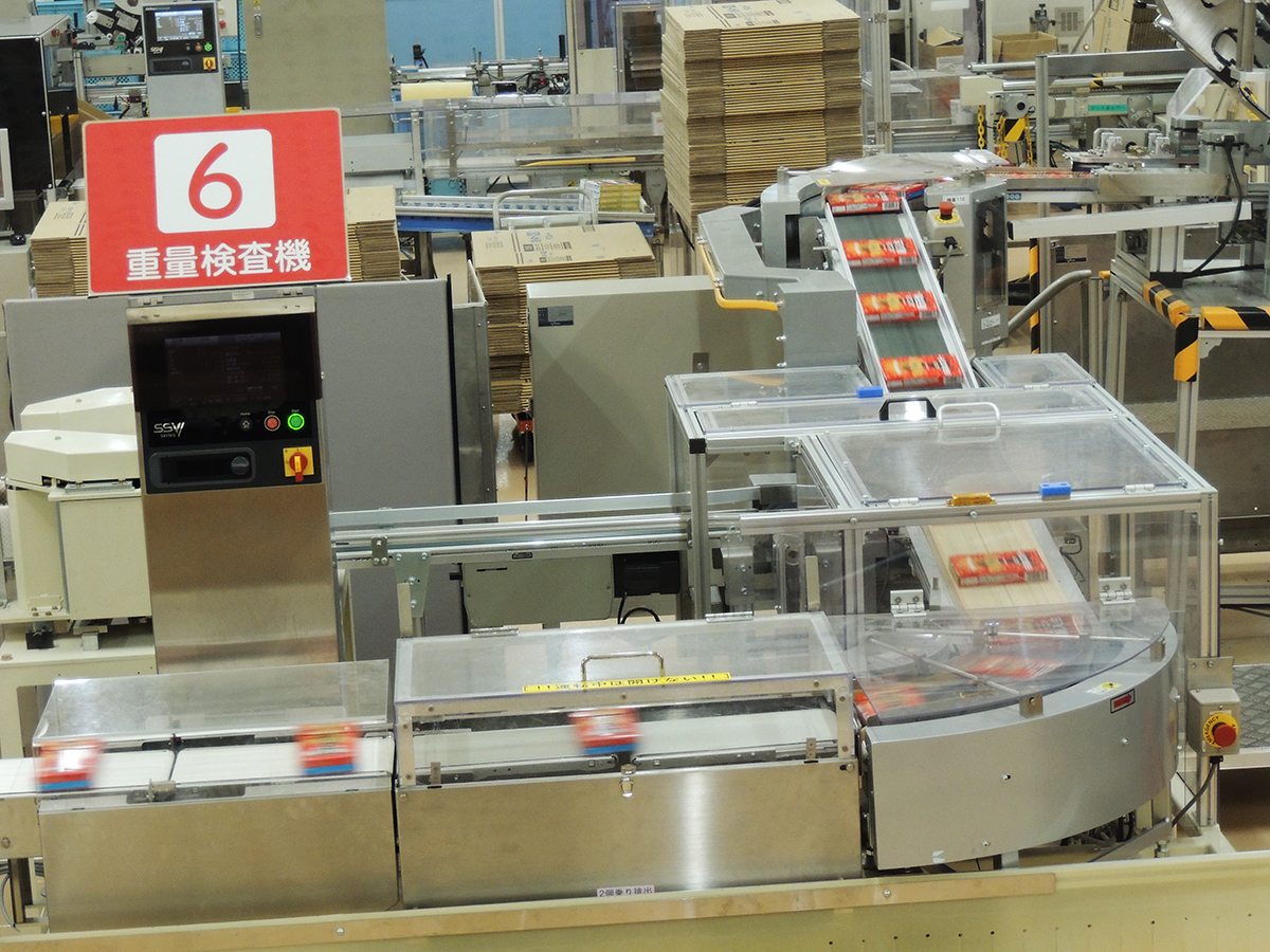 重さが間違っていないか検査する【6】重量検査機。高速でポッキーの箱が通り過ぎていきます