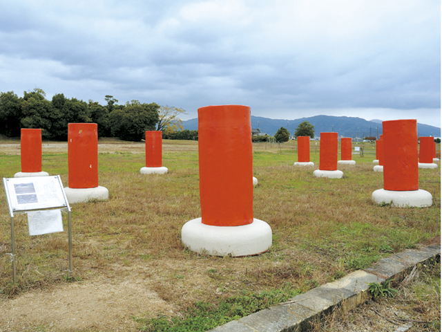 宮跡中心部の門があったことを示す模造柱。左後方の木が茂っている所は大極殿跡