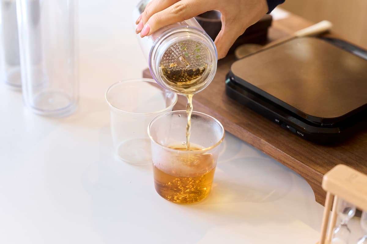 急須ボトルからコップにお茶を注いでいる