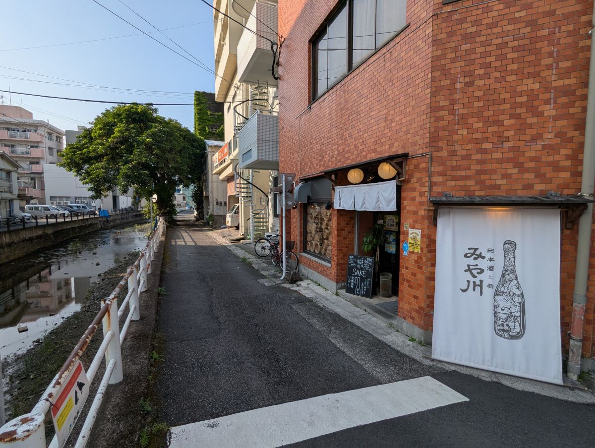 お酒のボトルをデザインしたイラストの暖簾。目の前には細い川も流れる