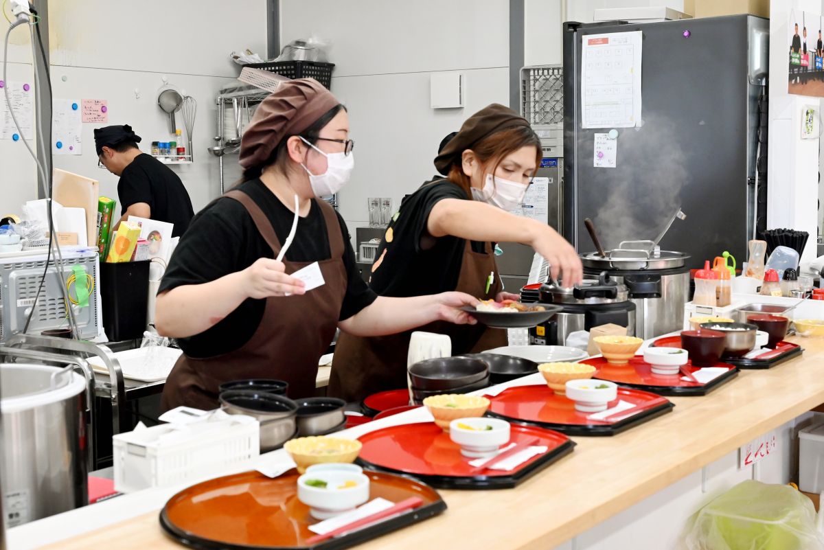 活気あふれるすずなり食堂のキッチン。カウンターに次々とお盆がセットされます    