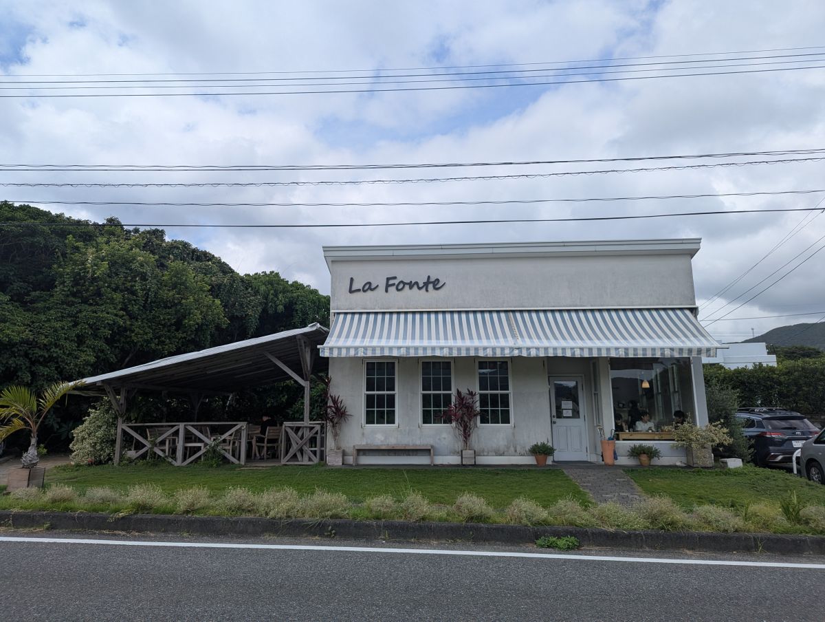 道路沿いに佇む白い小さな店。隣には森が見える。