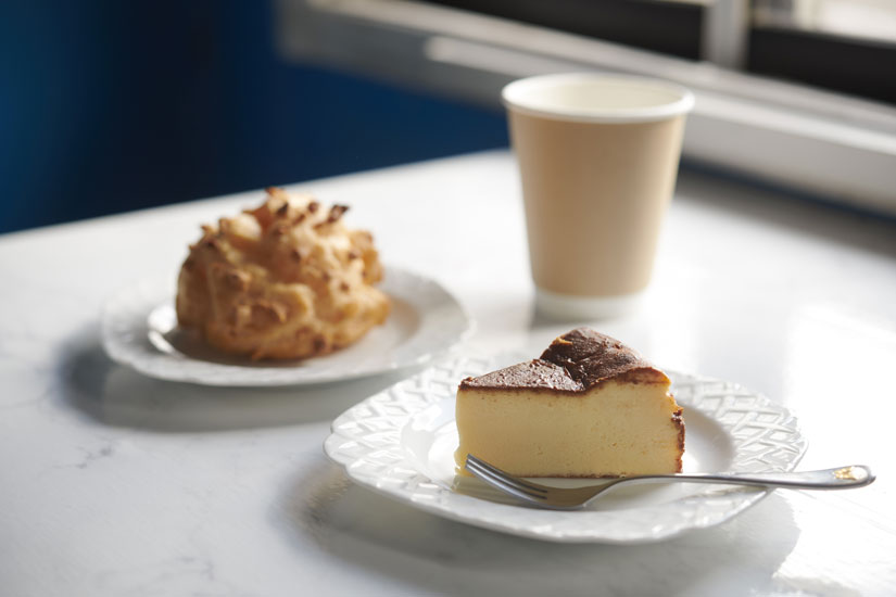 「バスク風チーズケーキ」480円（手前）、「平飼いたまごのシュークリーム」330円（左奥）。「ホットコーヒーS」400円はセルフ式のコーヒーマシンで淹れる