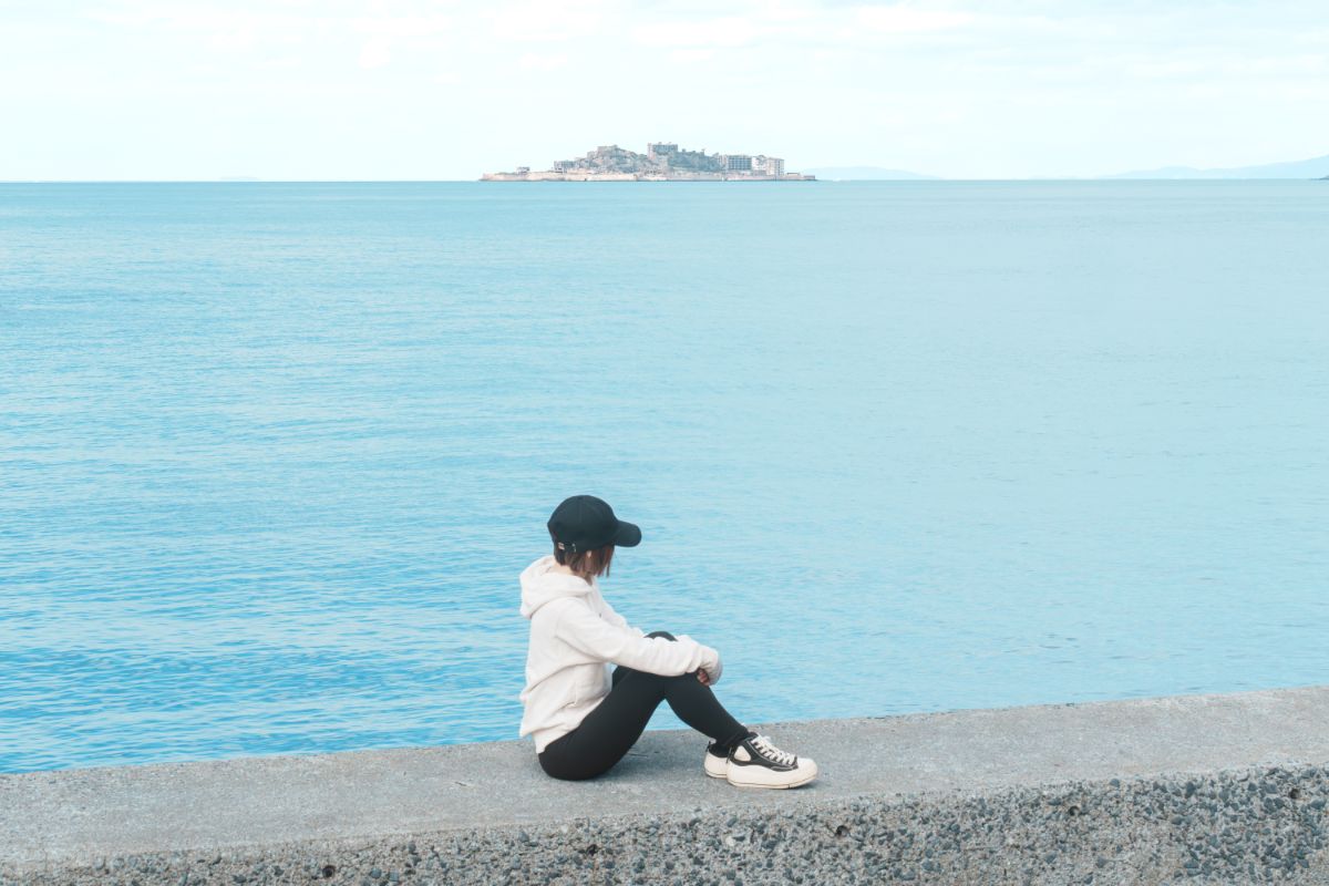 軍艦島の見える海沿いで座る女性