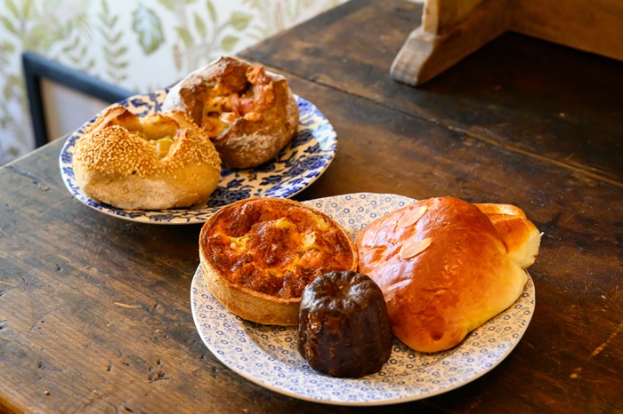 （手前の皿正面から時計回りに）「金澤カヌレ」350円、「キッシュ」550円、「クリームパン」370円、（奥の皿左）「五郎島金時とシルクスイート」390円、（同右）「加賀レンコンとチキン」380円